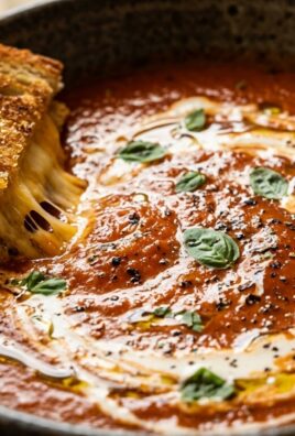 Ultra close-up macro of velvety creamy roasted tomato basil soup with grilled cheese dipper and cream swirl