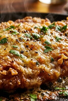 Ultra close-up macro food photography of sizzling crispy parmesan crusted chicken cutlet with melted parmigiano, cracked black pepper, and lemon