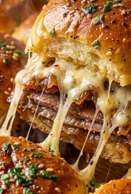 Ultra close-up macro food photography of Hawaiian roll French dip roast beef sliders pulling apart with melted cheese and garlic herb butter