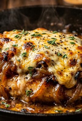 Ultra close-up macro food photography of golden seared chicken breasts smothered under caramelized sweet onions and melted bubbly Gruyere cheese